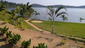 A serene lakeside view with a boat dock, palm trees, and a dirt path leading to a grassy area. - Palega Beach Inn (Boneza)