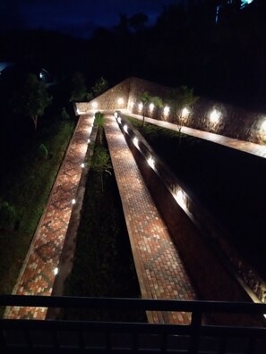 A pathway with brick paving and small lights along the sides, surrounded by greenery.