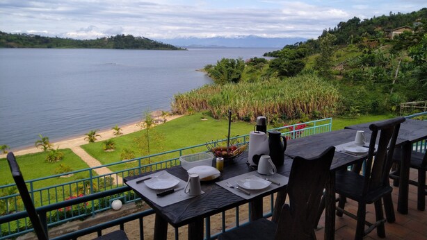 A dining table set with plates, cutlery, and a kettle, overlooking a lake and a lush green landscape. - Palega Beach Inn (Boneza)