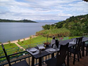 A dining table set with plates, cutlery, and a kettle, overlooking a lake and a lush green landscape.