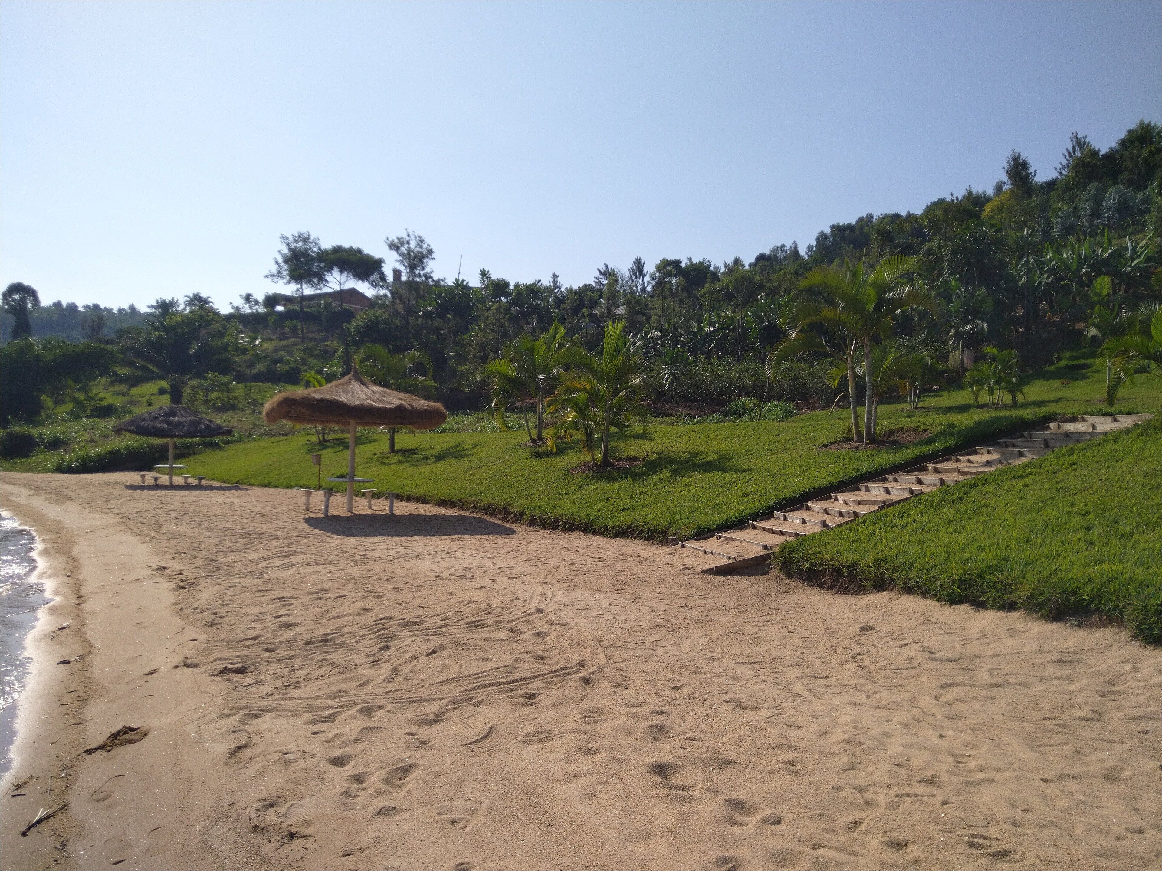 A beach with a thatched umbrella, a grassy area, and a pathway leading uphill.