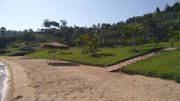 A beach with a thatched umbrella, a grassy area, and a pathway leading uphill.