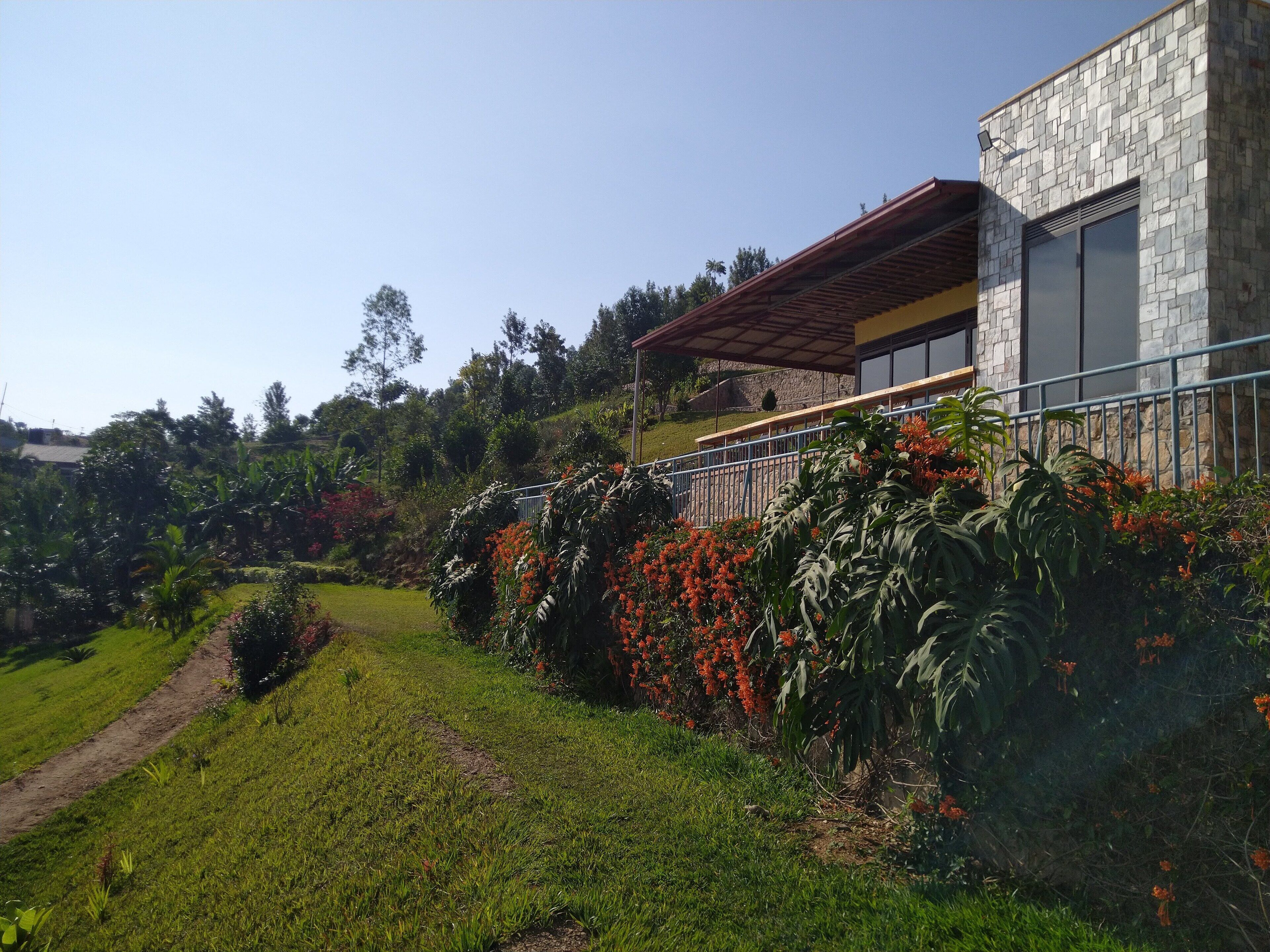 Une maison moderne avec une façade en pierre, un patio couvert et un jardin luxuriant agrémenté de fleurs rouges.