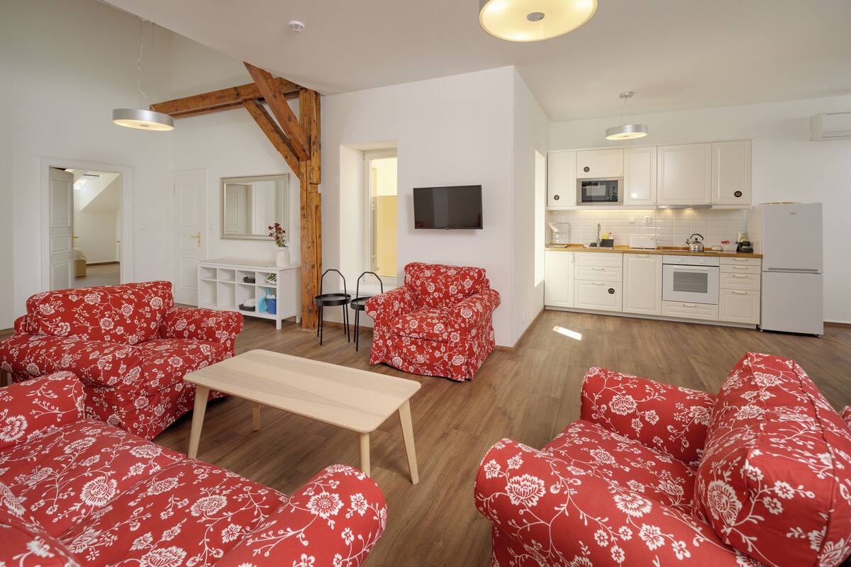Una sala de estar con sofás tapizados en estampado floral rojo, una mesa de centro de madera y un televisor montado en la pared.