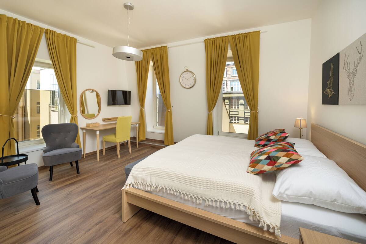 Habitación de hotel con cama, escritorio, silla, televisor y ventana con cortinas.