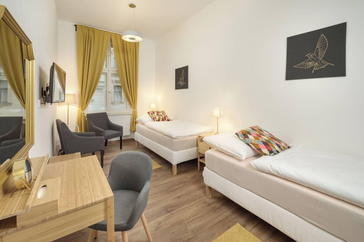 Habitación de hotel con cama, escritorio, silla, lámpara y un cuadro de un pájaro.