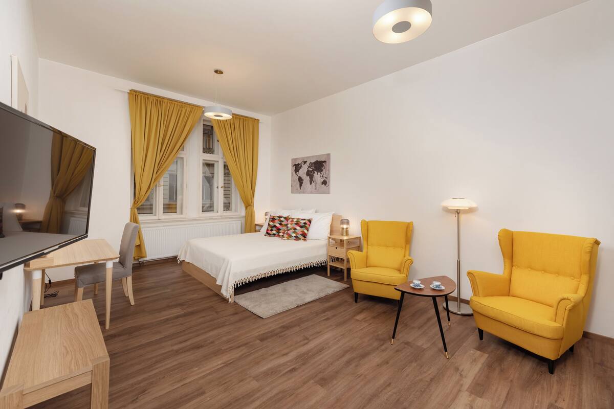 Una habitación de hotel moderna con una cama, dos sillones amarillos, un escritorio y un televisor.