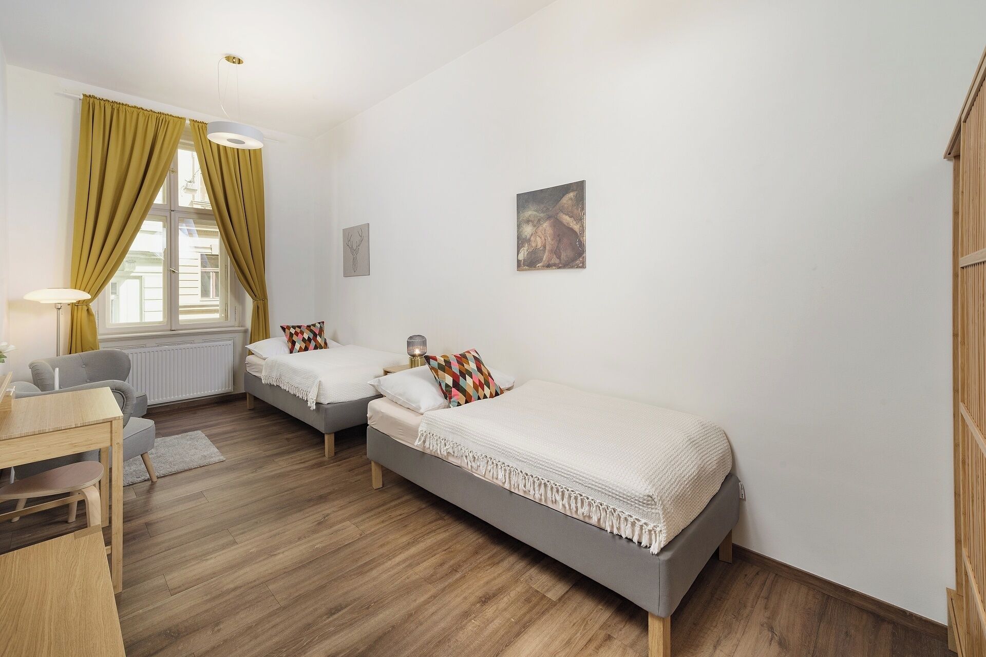 A bedroom with two single beds, a desk, a chair, and a window with curtains.
