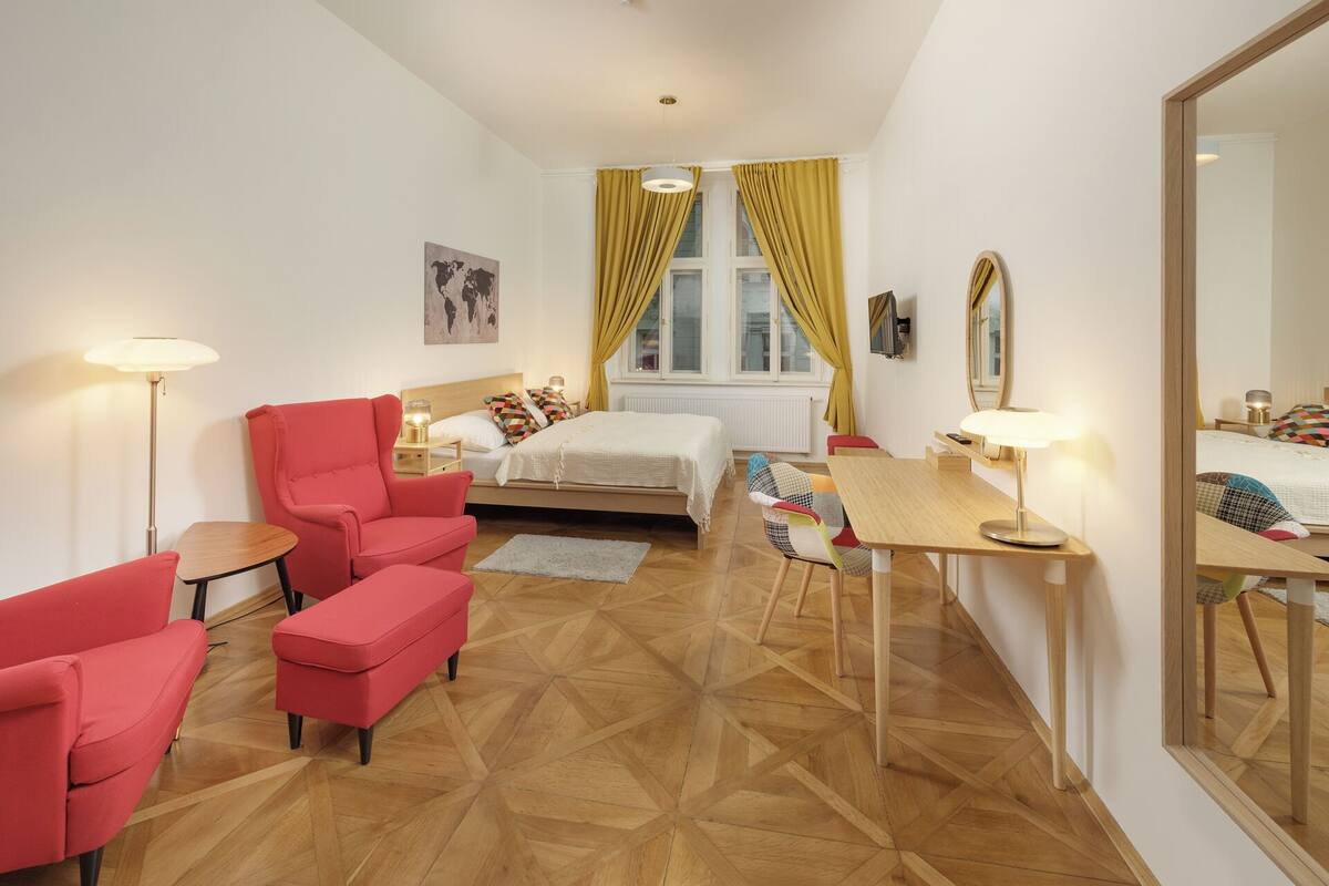 Habitación de hotel compacta con una cama, un escritorio, una silla y un sillón rojo.