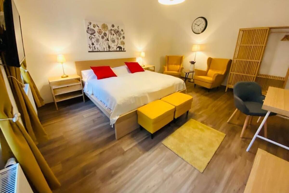 Un dormitorio con cama, mesitas de noche, una silla, un escritorio y un reloj en la pared.