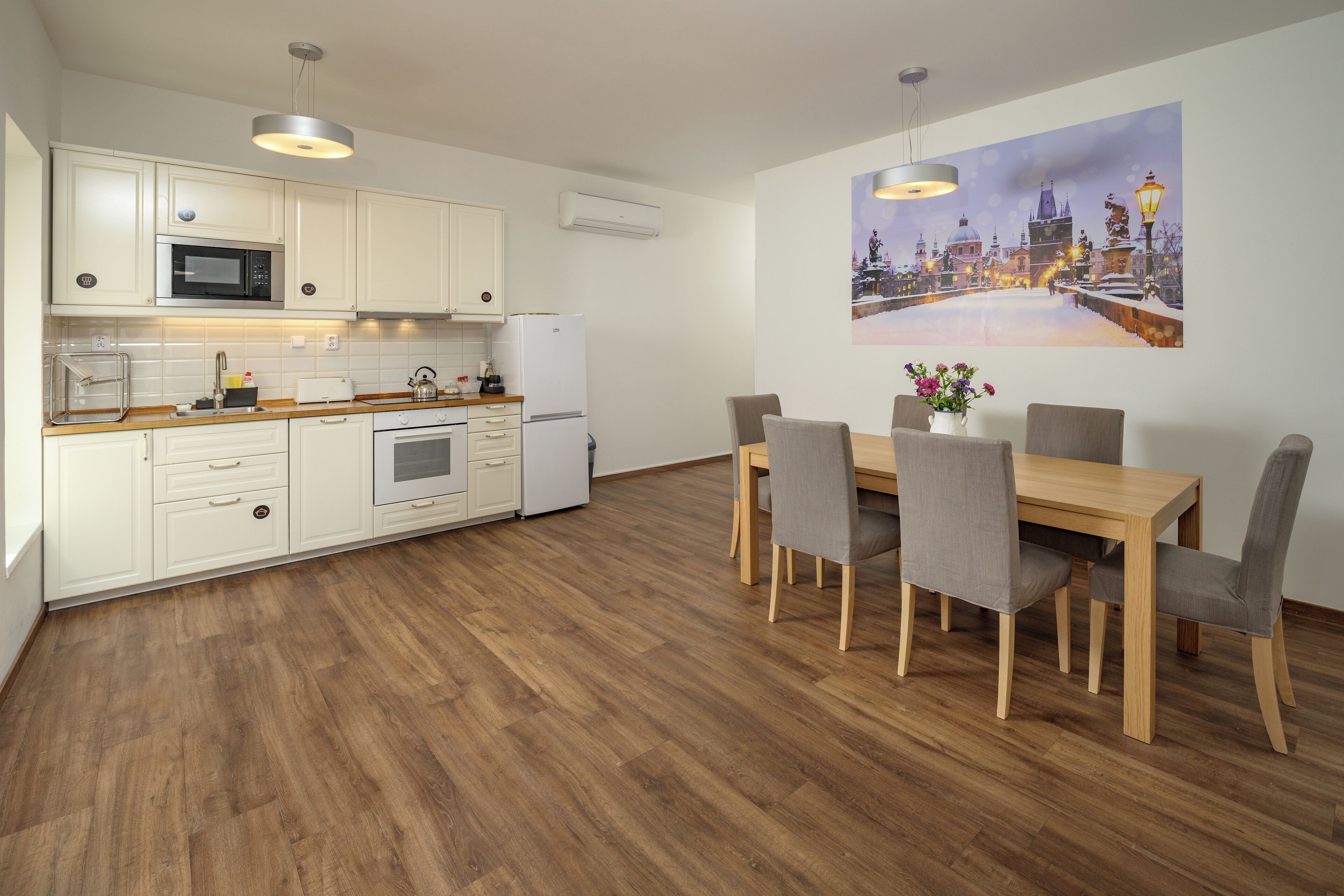 Una cocina moderna con armarios blancos, microondas, refrigerador y un comedor con mesa y sillas de madera.