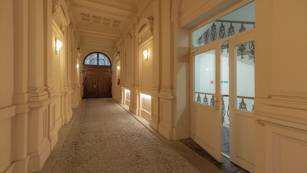 A corridor with ornate columns, a patterned floor, and a large arched window at the end. - Unesco Prague Apartments (Prague)
