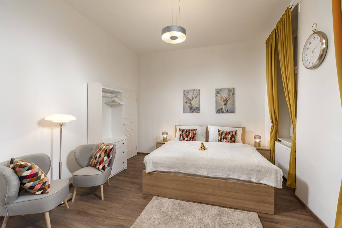 Un dormitorio moderno con una cama de madera, dos mesitas de noche, una lámpara de pie, una silla, un armario y dos cuadros colgados en la pared.