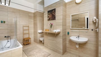 Un baño moderno con bañera, inodoro y lavamanos, que incluye un estante de madera con toallas y un espejo.