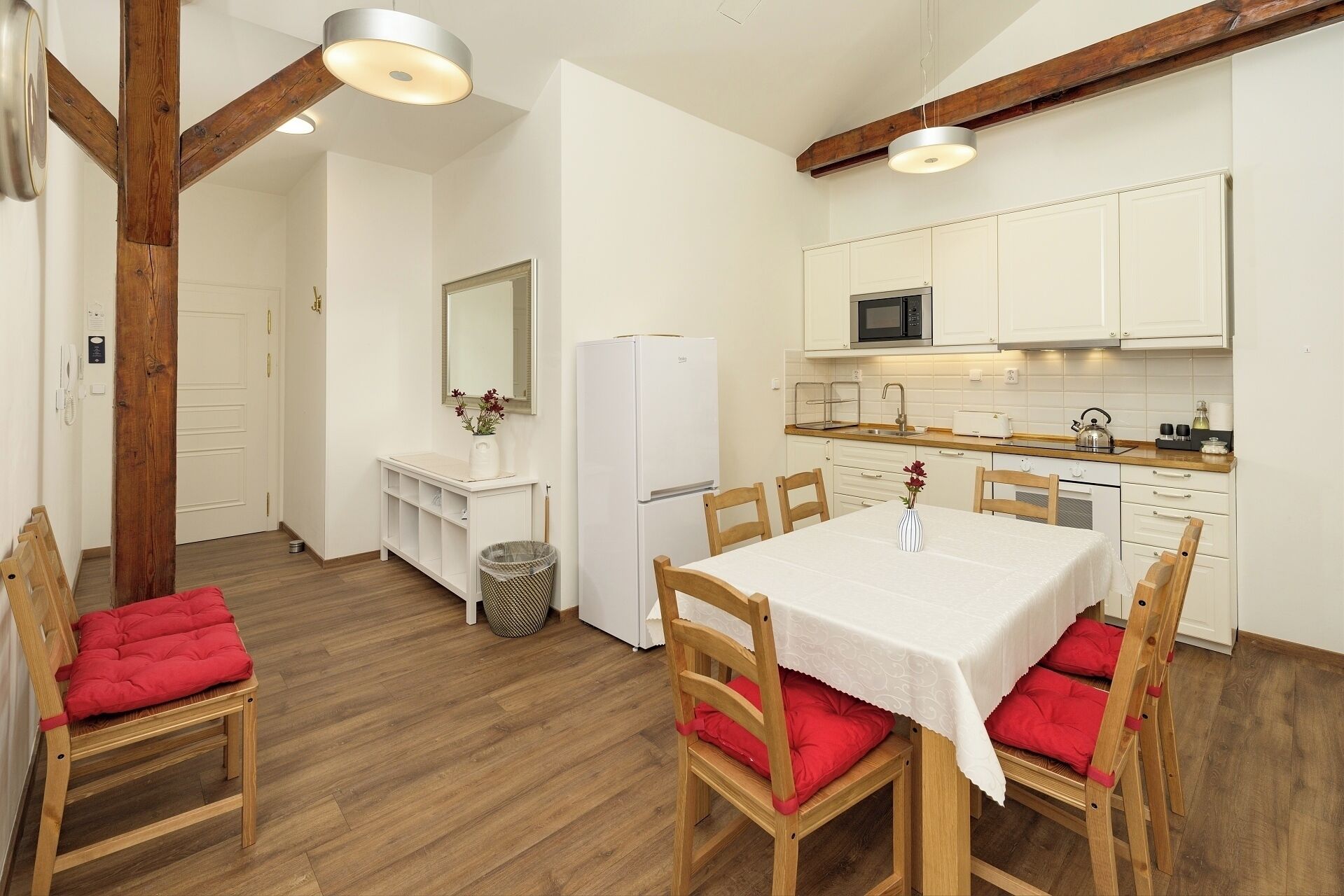 A compact kitchen with white cabinets, a microwave, and a refrigerator. There is a dining table with chairs and a vase with flowers.
