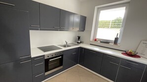 A modern kitchen with dark cabinets, a white countertop, a built-in oven, and a window providing natural light. - Traumhafter Lieblingsplatz in Pfullendorf am Nördlichen Bodensee (Pfullendorf)