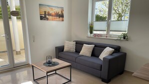 A modern living room with a grey sofa, a wooden coffee table, and a cityscape painting on the wall. - Traumhafter Lieblingsplatz in Pfullendorf am Nördlichen Bodensee (Pfullendorf)