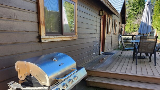 A wooden cabin with a barbecue grill, a patio with a table and chairs, and a view of the surrounding forest. - Escape to Nature: Charming 3-Bedroom Cabin near Trinity Lake (Trinity Center)