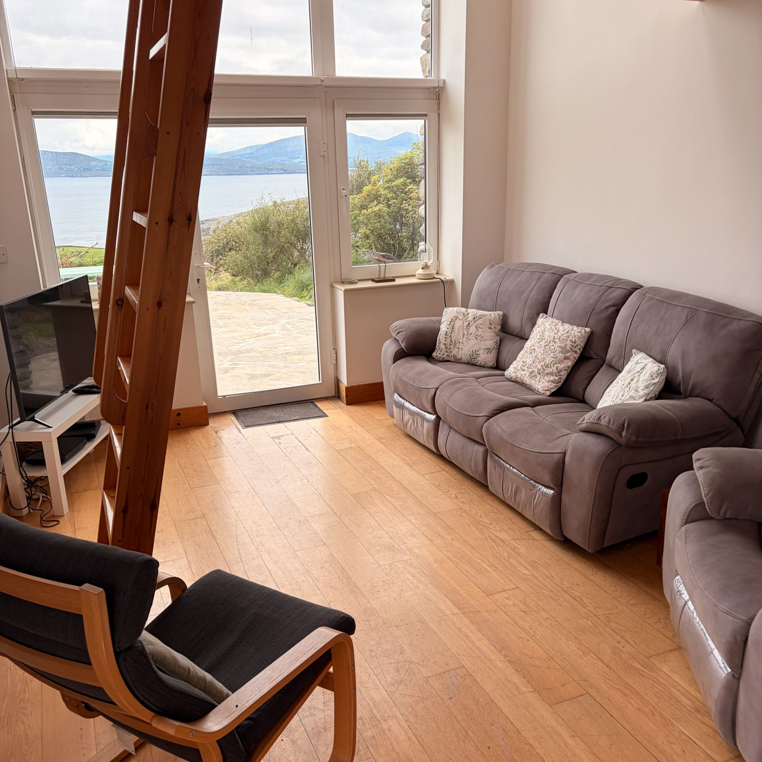 A living room with a grey sofa, a wooden chair, and a television on a stand.