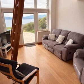 A living room with a grey sofa, a wooden chair, and a television on a stand.