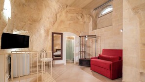 Una habitación amplia con pared de piedra, un sofá rojo, un televisor montado en la pared y un aparador de vidrio.