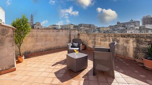 Terraza en la azotea con mobiliario de mimbre, una planta en maceta y una vista despejada del paisaje urbano.
