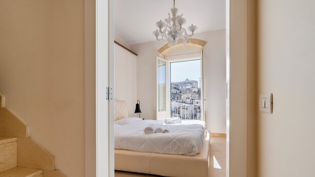 Un dormitorio con una cama grande, una araña de cristal y vistas a la ciudad a través de una ventana.