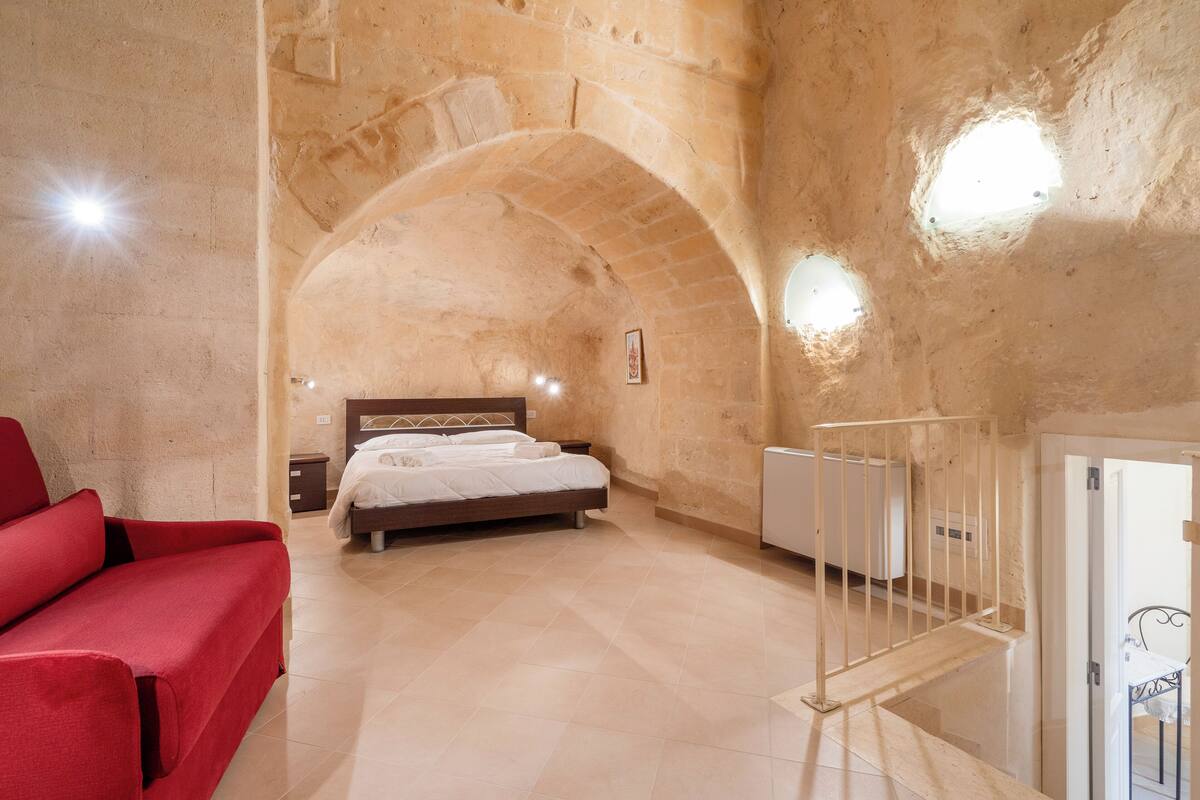 A bedroom with a bed, a red sofa, a staircase, and a stone wall.