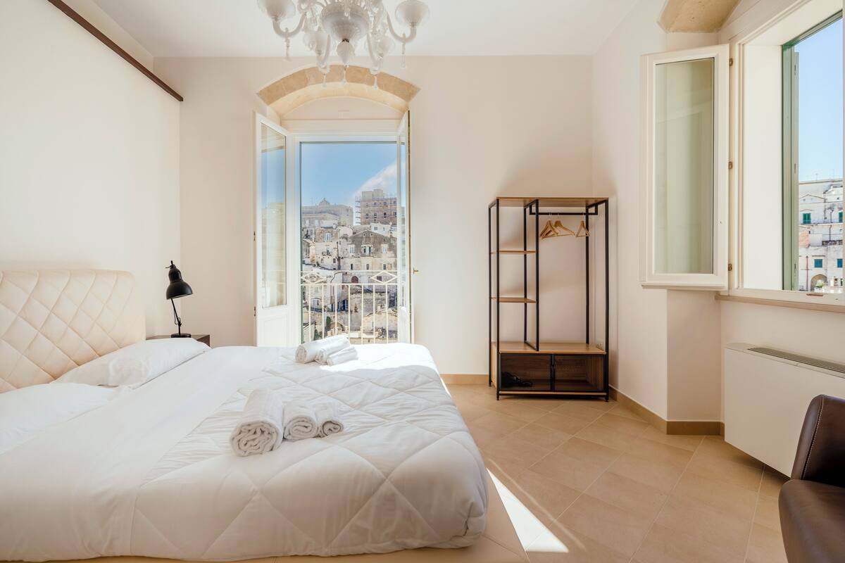 A hotel room with a bed, a hanging clothes rack, a radiator, and a view of the city.