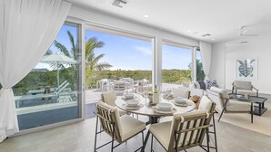 Un comedor moderno con una mesa grande dispuesta para seis personas, con vistas a una terraza exterior con palmeras y cielo despejado.