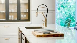 Eine moderne Küche mit weißer Arbeitsplatte, einem goldenen Wasserhahn und Blick ins Grüne.