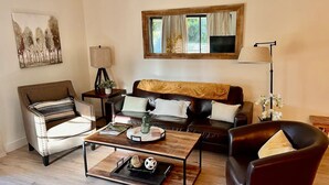 Ein Wohnzimmer mit Sofa, Sessel, Couchtisch und einem Gemälde an der Wand.