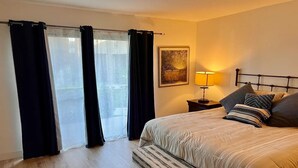 Ein Schlafzimmer mit einem Bett, einer Sitzbank, einem Nachttisch, einer Lampe und einem Bild an der Wand.