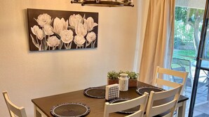 Ein Essbereich mit einem Holztisch, vier Stühlen, einer Chandelierleuchte, einem Blumenbild und Blick durch eine Glastür.