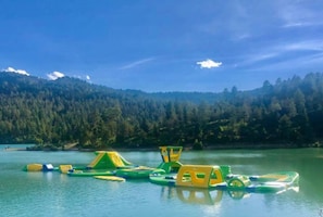 Ein See mit schwimmenden Spielgeräten und einer bewaldeten Hügelkulisse im Hintergrund.