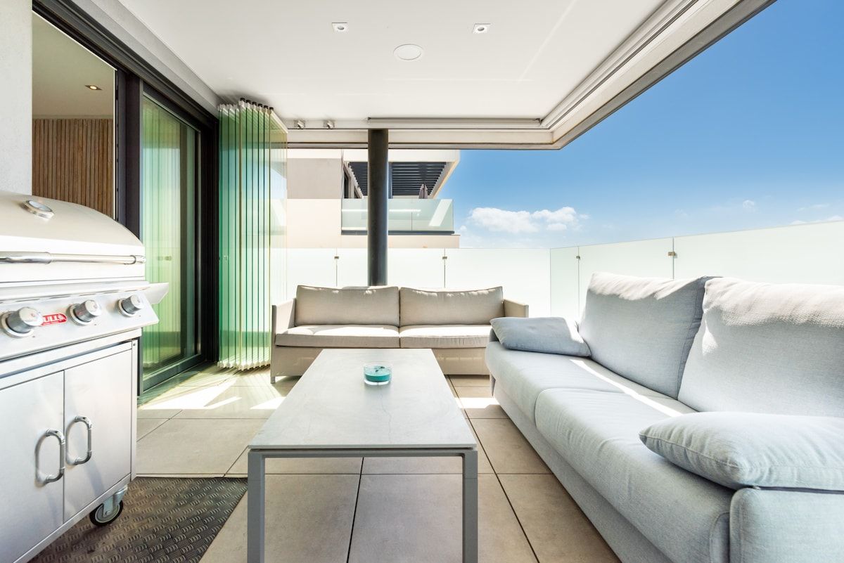 A modern outdoor living area with a sofa, a coffee table, and a grill.