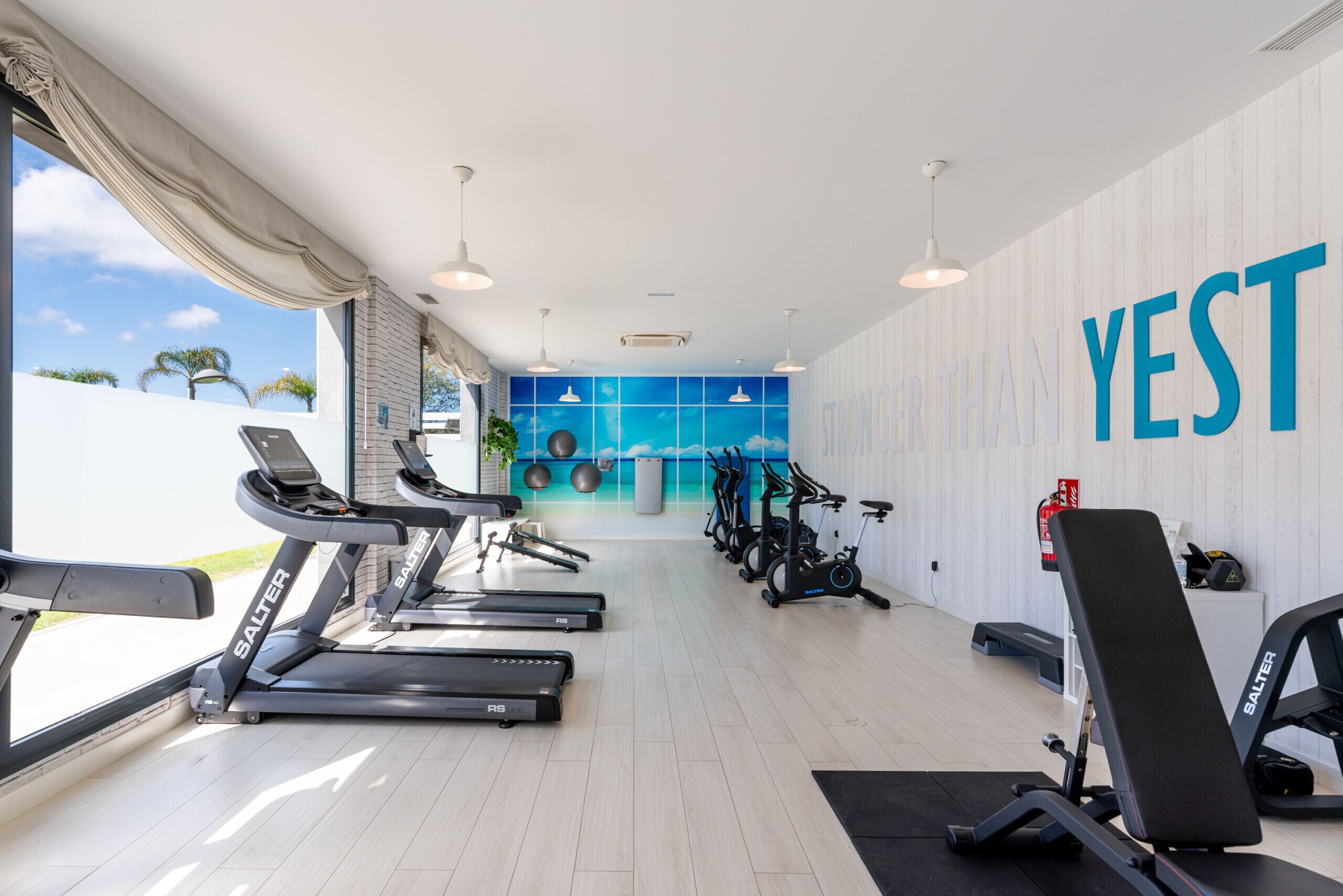 A modern gym with treadmills, stationary bikes, and a wall with the word "YEST".