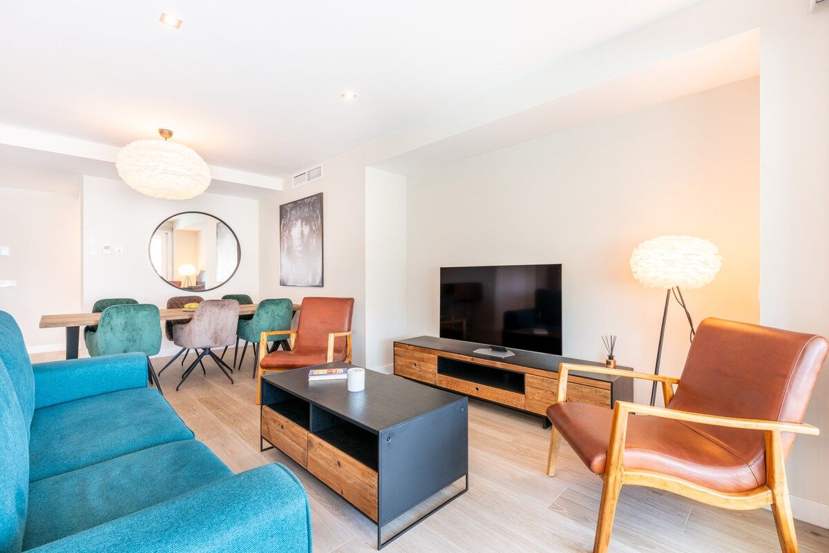 A modern living room with a sofa, coffee table, TV, and a dining area with chairs and a table.
