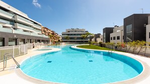 A modern hotel with a large outdoor swimming pool, a covered terrace, and a view of the surrounding buildings.