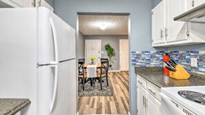 A kitchen with white cabinets, a granite countertop, and a backsplash with blue and white tiles. - Condo Comforts of HOMME (Kannapolis)