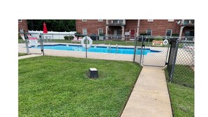 A fenced pool area with a concrete pathway leading to a building. - Condo Comforts of HOMME (Kannapolis)