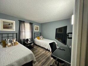 A hotel room with two beds, a desk, a chair, a TV, and a window with curtains.
