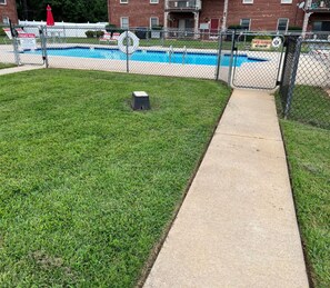 Ein eingezäuntes Pool-Gelände mit einem Betonweg, der zu einem Gebäude führt.