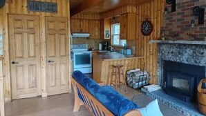 A cabin interior with a wooden interior, a fireplace, a kitchen area with a stove and sink, and a bench. - Le Rustique avec lac privé (Château-Richer)