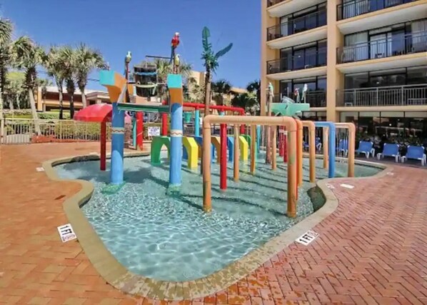 A water play area with colorful structures and a pool, surrounded by a brick walkway and palm trees. - Wonderful Oceanview 1 bedroom (Myrtle Beach)