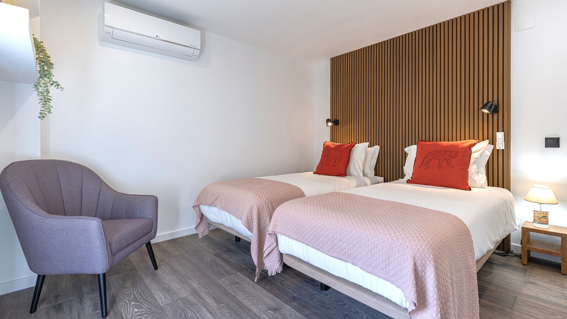 Habitación de hotel con dos camas, una silla, aire acondicionado instalado en la pared y una mesita de noche con lámpara.