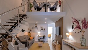 A modern apartment with a staircase, a living area with a sofa and coffee table, a dining area with a table and chairs, and a kitchen area.
