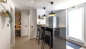 A modern kitchen with a bar area, featuring pendant lights, a refrigerator with magnets, and a door with an emergency exit sign.