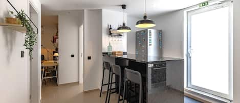 A modern kitchen with a bar area, featuring pendant lights, a refrigerator with magnets, and a door with an emergency exit sign.