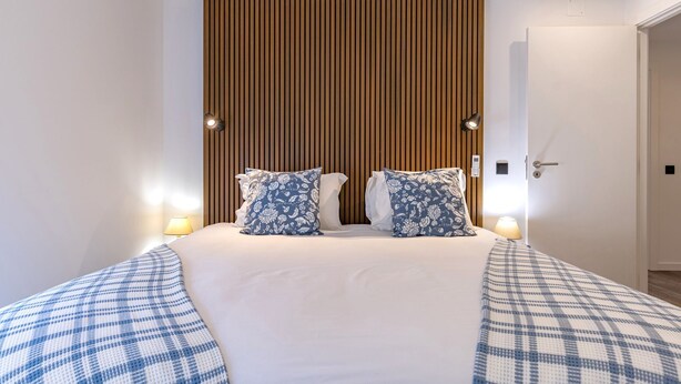 A hotel room with a large bed, two bedside lamps, a wooden slat wall, and a door to the right.